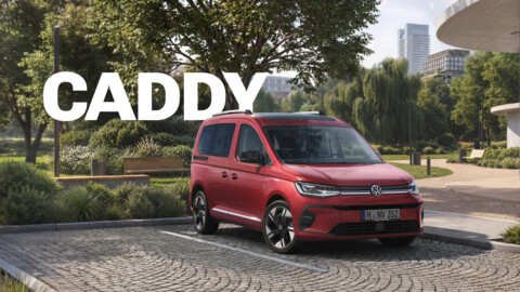 Roter Volkswagen Caddy geparkt vor einem modernen Gebäude in einer grünen Parkanlage, mit dem Schriftzug „CADDY“.