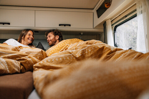 Mann und Frau lachen gemeinsam im Bett eines integrierten Wohnmobils